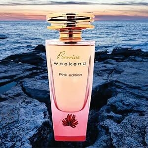 Pink perfume bottle with gold cap against sunset ocean backdrop. Bottle has floral accent at base and 'Breezes weekend' text visible.