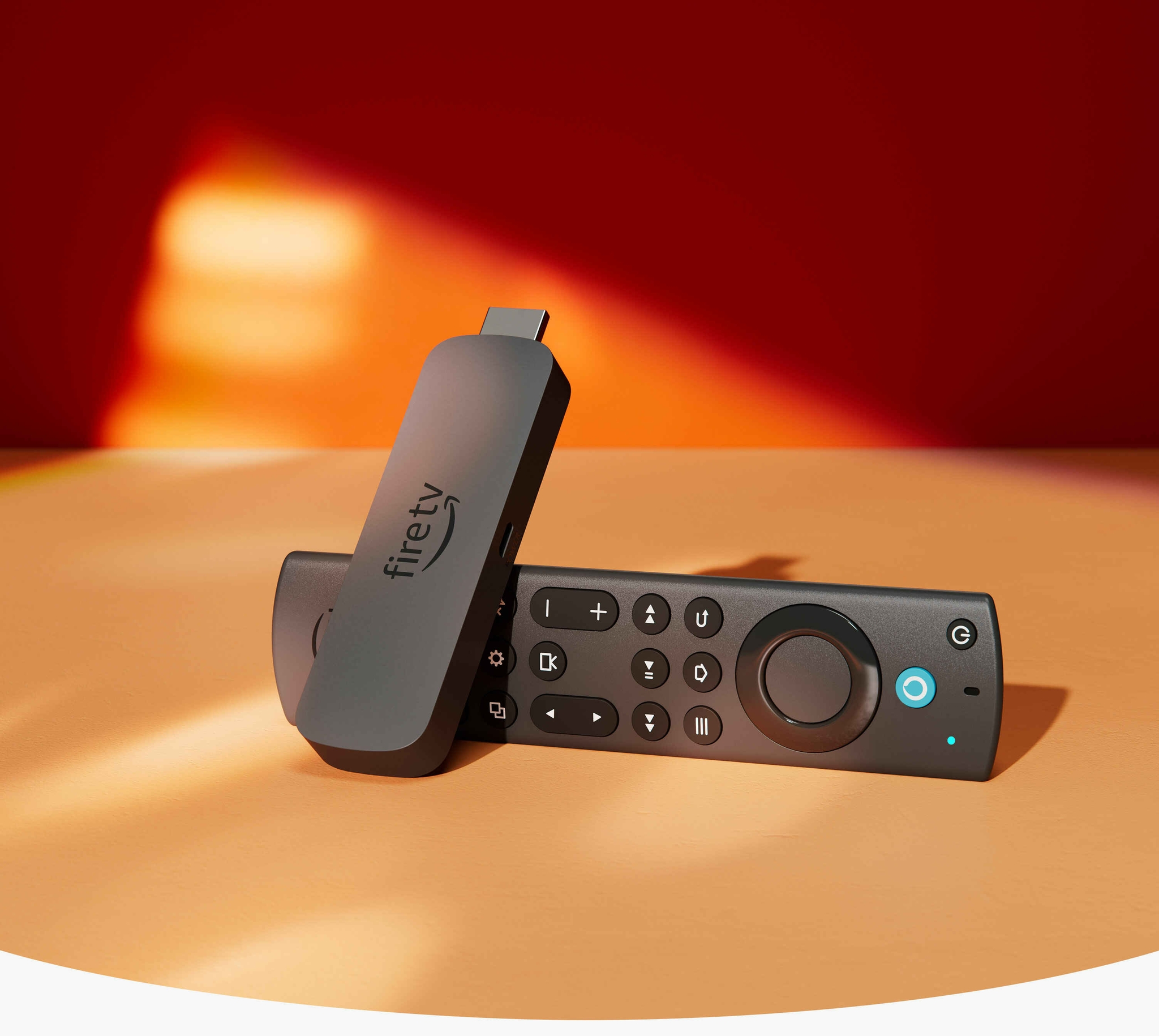 Fire TV Stick (4k Max): rectangular device with an HDMI connector on one end and a USB-C socket on the side, with Fire TV Alexa Voice Remote Enhanced, with a navigation ring and buttons on the front and a rounded back.